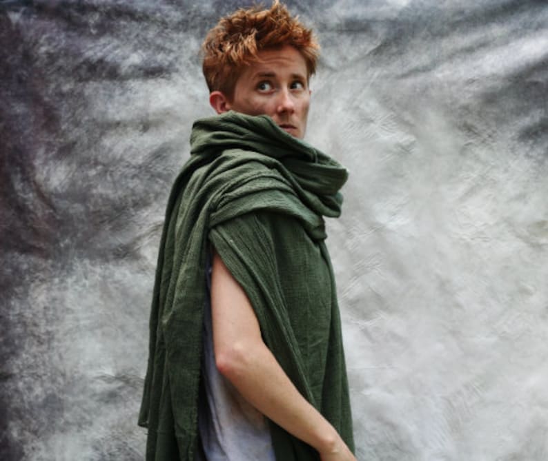May include: A dark green cape with a draped design. The cape is made of a textured fabric and is wrapped around the shoulders and neck. The person in the image is wearing a gray shirt underneath the cape.