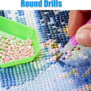 May include: A diamond painting project in progress is shown. A green tray holds light pink round drills, a pink stylus is in use, and a canvas is partially complete with various coloured drills. The text "Round Drills" is at the top of the image.