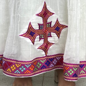 May include: White skirt with a pink and gold embroidered cross design and a colorful geometric trim.