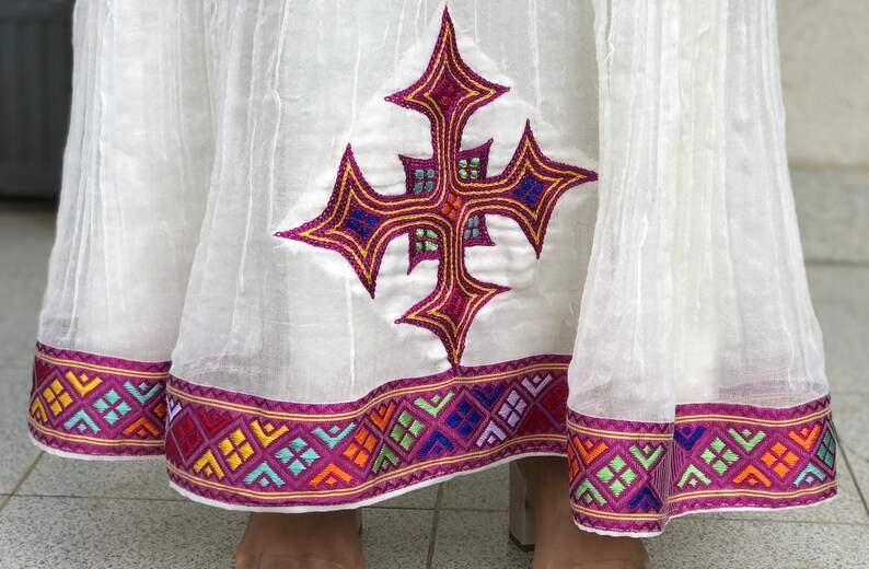 May include: White skirt with a pink and gold embroidered cross design and a colorful geometric trim.