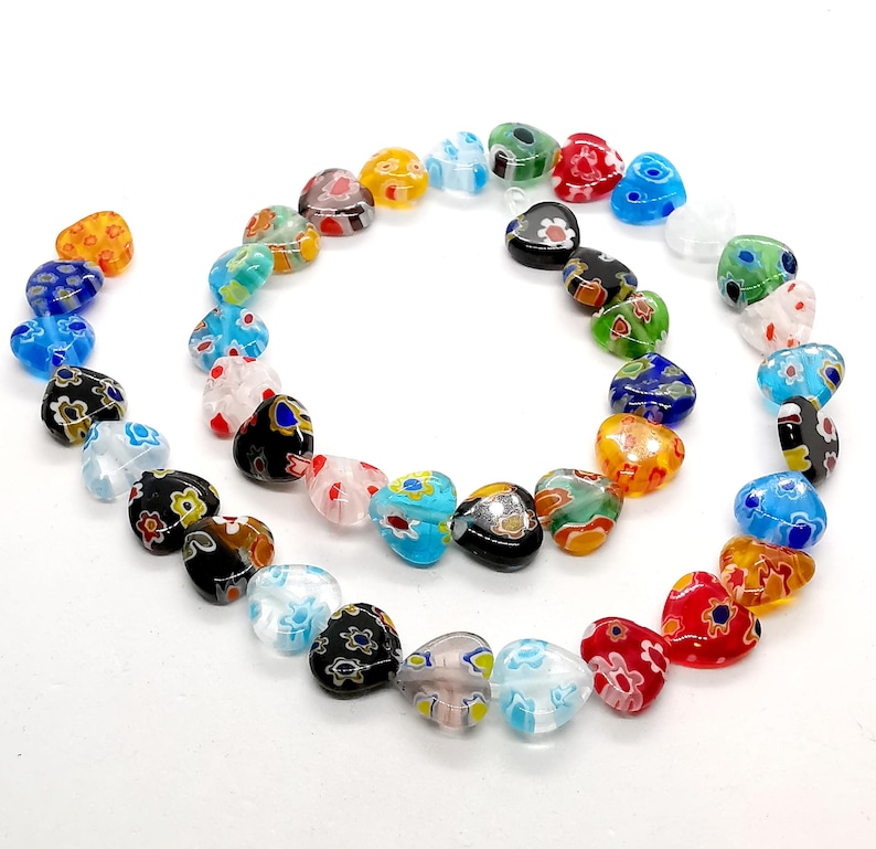 May include: A strand of colorful glass heart beads with floral patterns. The beads are strung on a clear thread and are arranged in a circle.