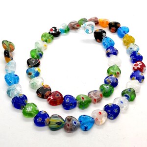 May include: A strand of colorful heart-shaped glass beads with floral patterns. The beads are strung on a clear thread and are arranged in a circle.