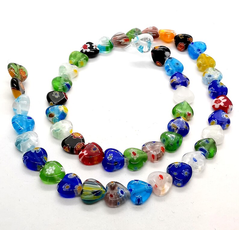 May include: A strand of colorful heart-shaped glass beads with floral patterns. The beads are strung on a clear thread and are arranged in a circle.