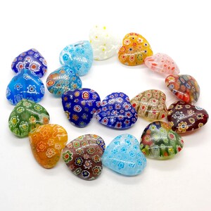May include: A collection of 15 heart-shaped glass beads with various colorful floral patterns. The beads are arranged in a circle on a white background.