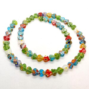 May include: A strand of colorful heart-shaped glass beads. The beads are made of clear glass with a variety of floral patterns in shades of red, green, blue, and white.
