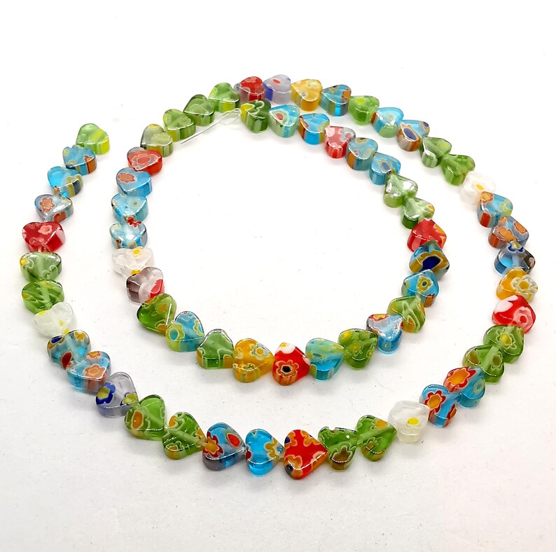 May include: A strand of colorful heart-shaped glass beads. The beads are made of clear glass with a variety of floral patterns in shades of red, green, blue, and white.