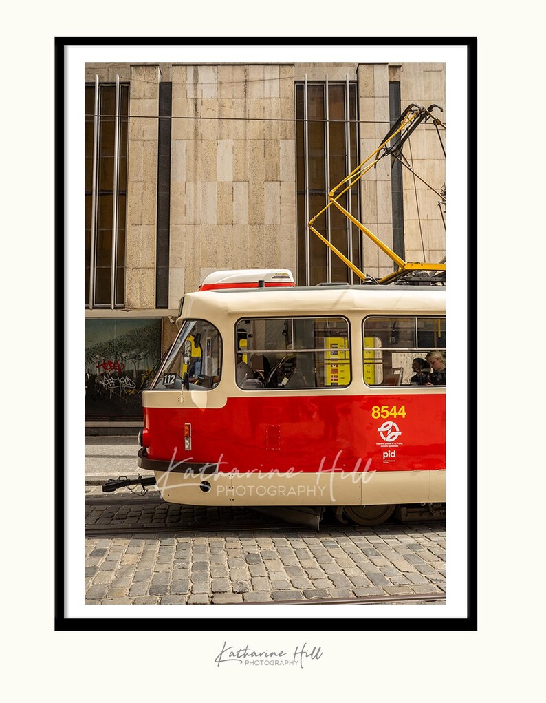May include: A framed photograph of a red and cream tram in a city. The tram has the number 8544 on its side. The photograph is signed "Katharine Hill PHOTOGRAPHY".