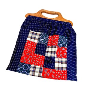May include: A fabric handbag featuring a dark blue exterior with a white polka dot pattern and a central patchwork panel. The panel consists of red floral, blue geometric, and plaid fabric squares. The bag has a curved, light brown wooden handle.