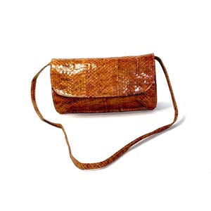 May include: A rectangular shoulder bag featuring a textured, brown snakeskin-patterned exterior. The bag has a fold-over flap closure and a thin, matching brown shoulder strap. The surface displays a distinct, repeating scale-like pattern.