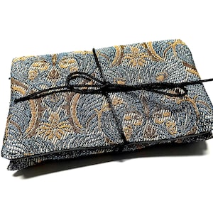 May include: A folded textile item with a detailed floral pattern in shades of blue, brown, and gold. The item is secured with a black string tied in a bow. The fabric has a textured appearance.