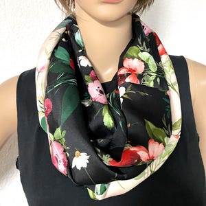 Könnte beinhalten: Ein schwarzer Infinity-Schal mit einem lebendigen Blumenmuster aus rosa, roten und weißen Blüten, die mit grünen Blättern durchsetzt sind. Der Schal hat eine glatte, satinartige Oberfläche und ist in einer kreisförmigen Schlaufe drapiert.