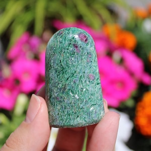 Puede incluir: Una punta de cristal de zoisita rubí verde y rosa. El cristal es liso y pulido, con una parte superior redondeada y una base plana.