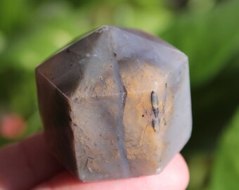 May include: A gray, brown, and white agate crystal shaped like a hexagon. The crystal is smooth and polished.