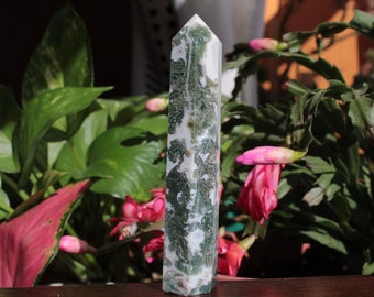 May include: A white and green moss agate crystal point, also known as a green phantom crystal, with a pointed tip and a smooth, polished surface.