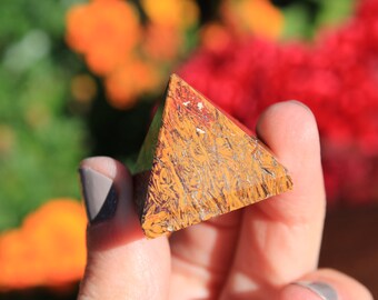 May include: A pyramid-shaped crystal with a brown, orange, and red color pattern. The crystal is made of tiger's eye stone.