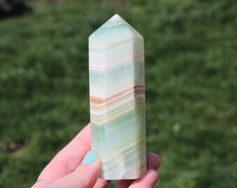 May include: A green, white, and brown banded onyx crystal point. The crystal is polished and has a pointed tip.