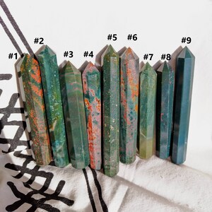 May include: Nine polished green, red, and brown jasper crystal points, numbered 1 through 9, arranged in a row on a white fabric background.