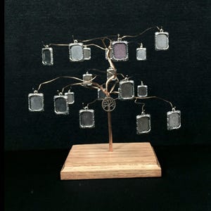 May include: A silver wire tree with a wooden base holds 14 small silver picture frames. The frames are hanging from the branches of the tree. The tree is on a black background.