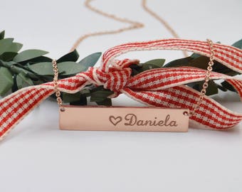 Könnte beinhalten: Eine Halskette aus Roségold mit einem Bar-Anhänger, der mit einem Herz und dem Namen "Daniela" graviert ist. Die Halskette wird auf einem rot-weiß karierten Band präsentiert.
