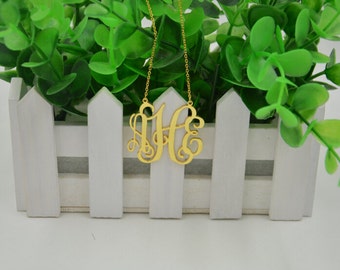 Puede incluir: Un collar de color dorado con un colgante de monograma con las letras "JHE" en escritura cursiva.