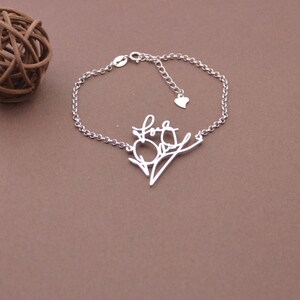 May include: A silver bracelet with a delicate chain and a charm that says "Love" in cursive script. The charm is shaped like a branch with a heart at the end.