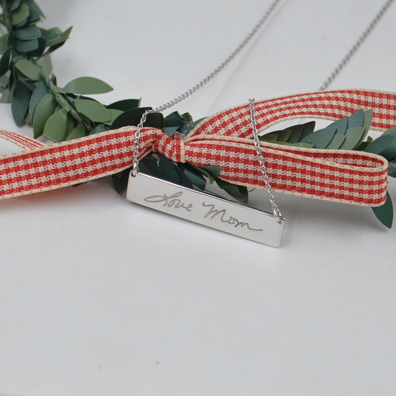 May include: Silver necklace with a rectangular pendant engraved with the handwritten message "Love Mom".