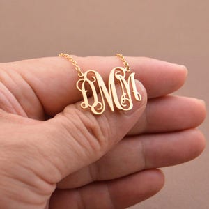 以下が含まれることがあります： 「DMM」の文字が筆記体で書かれたモノグラムペンダントが付いたゴールドネックレス