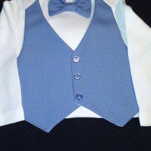 以下が含まれることがあります： 白いボディスーツに青いベストと青い蝶ネクタイをつけた赤ちゃん。ベストには5つのボタンがついています。