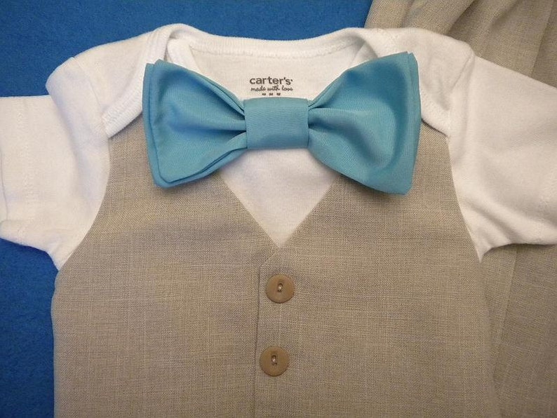 May include: A white bodysuit with a light blue bow tie and a beige linen vest with two brown buttons. The bodysuit has the text "carter's made with love" printed on the front.
