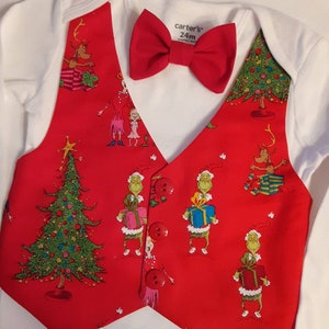 May include: A white long-sleeve bodysuit with a red vest overlay featuring a Grinch and Christmas tree print. The vest has three red buttons and is paired with a matching red bow tie. The bodysuit label reads carter's 24m.