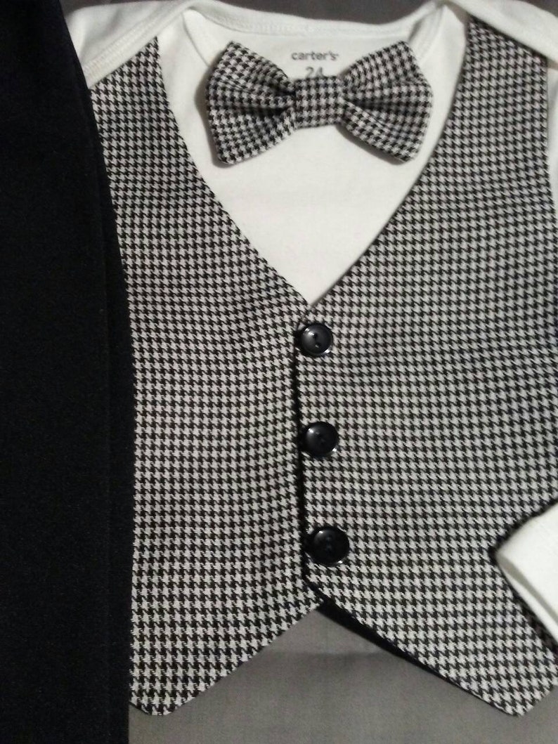May include: A black and white houndstooth vest with three black buttons. The vest is paired with a white bodysuit and a black and white houndstooth bow tie. The bodysuit has a label that reads "carter's" and "24".