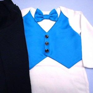 Może przedstawiać: Str&oacute;j dla chłopca z białą koszulą z długim rękawem, niebieską kamizelką i czarnymi spodniami. Kamizelka ma czarne guziki i pasujący niebieski krawat.