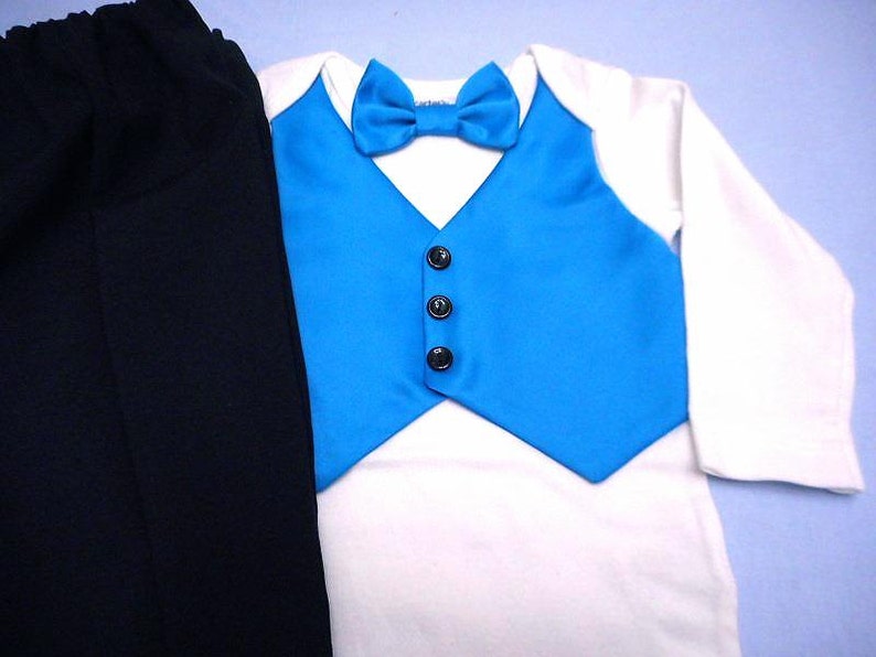 Może przedstawiać: Str&oacute;j dla chłopca z białą koszulą z długim rękawem, niebieską kamizelką i czarnymi spodniami. Kamizelka ma czarne guziki i pasujący niebieski krawat.