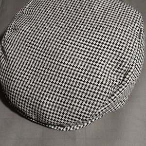 May include: A black and white houndstooth patterned cap. The cap is made of a soft, textured fabric.
