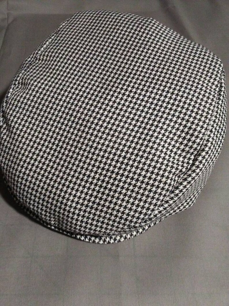 May include: A black and white houndstooth patterned cap. The cap is made of a soft, textured fabric.