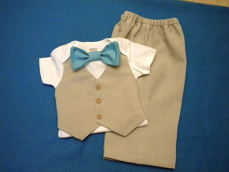 May include: A baby outfit set with a white onesie, a beige vest, and beige pants. The onesie has a blue bow tie.
