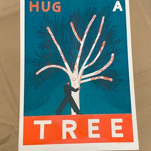 May include: A teal blue poster with the text "HUG A TREE" in white letters. A person is hugging a white tree with red branches against a teal blue background. The poster is signed "MAX MACKEN" in the bottom right corner.