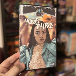 May include: A VHS tape for "Poor Things" from the Brainbuster Monsters collection. The cover features a woman in a blue jacket and a ruffled white shirt. The title is in large, bold letters.