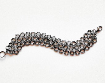 May include: A silver chain bracelet with a clasp closure. The chain is made of multiple rows of small, interconnected rings.