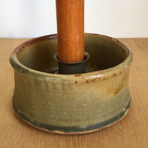 May include: A ceramic candle holder with a green glaze and a brown wooden candle. The holder has a metal ring to hold the candle in place.
