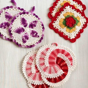 May include: A collection of handmade crochet pot holders in various designs. The pot holders feature white, red, pink, purple, and yellow colors. One set has a floral design, another has a spiral pattern, and the third has a square shape with a flower in the center.