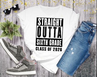 May include: A white t-shirt with the text "STRAIGHT OUTTA SIXTH GRADE CLASS OF 2026" in black. The shirt is paired with blue jeans and gray sneakers. Sunglasses and a small plant are also in the image.