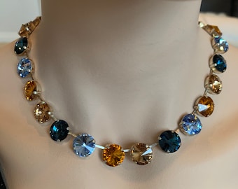 May include: A silver necklace with a graduated ombre design featuring blue, topaz, and amber crystal stones.