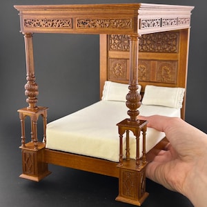 May include: A miniature wooden four-poster bed with intricate carvings. The bed frame is a warm brown color, with a white mattress and two white pillows. The bed has decorative posts and a detailed headboard.