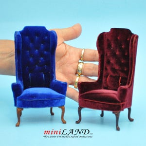 May include: Two miniature velvet chairs, one blue and one burgundy, with a tufted back and a high back. The chairs have wooden legs and are sitting on a light blue surface.