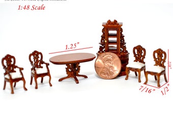 May include: A miniature dining set with a 1.25 inch oval table, four chairs, and a small cabinet with shelves. The set is made of wood and has a dark brown finish. The chairs have white cushions. The set is 1:48 scale.