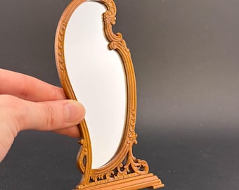 May include: A wooden, ornate, free-standing mirror with an oval-shaped reflective surface. The mirror has a brown finish and intricate carvings.