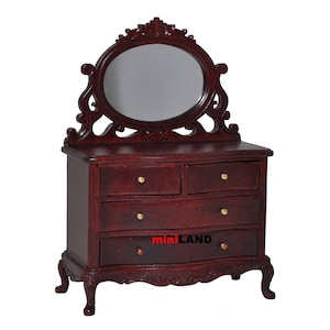 May include: A mahogany wood dresser with an oval mirror and four drawers. The dresser has ornate carvings and gold-colored knobs. The dresser is a miniature piece of furniture.