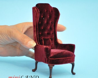 May include: A miniature burgundy velvet armchair with a high back and tufted upholstery. The chair has four carved wooden legs and a small cushion on the back.