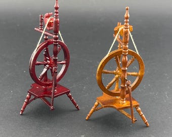 May include: Two miniature wooden spinning wheels, one red and one brown, with string attached to the wheels. The wheels have a traditional design with spokes and a central hub.